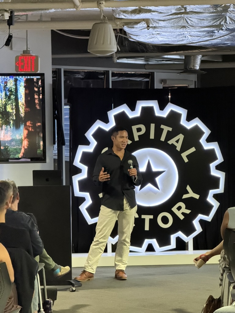 Hugh Chin presenting on stage at Capital Factory with a microphone