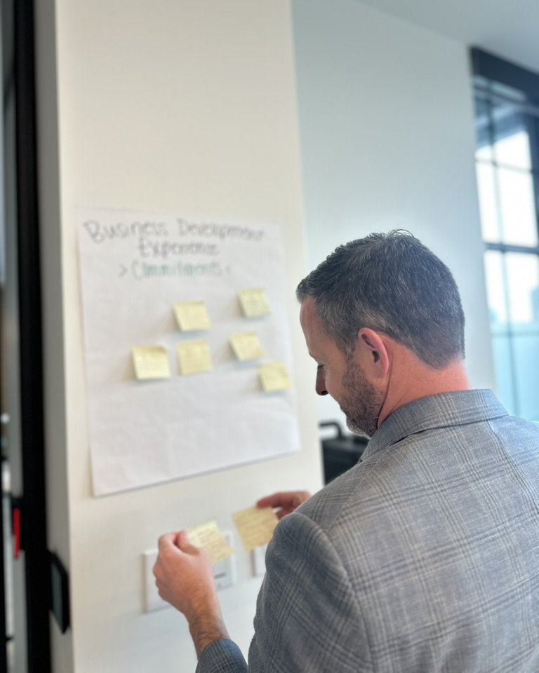Participant placing sticky note commitments on a workshop board